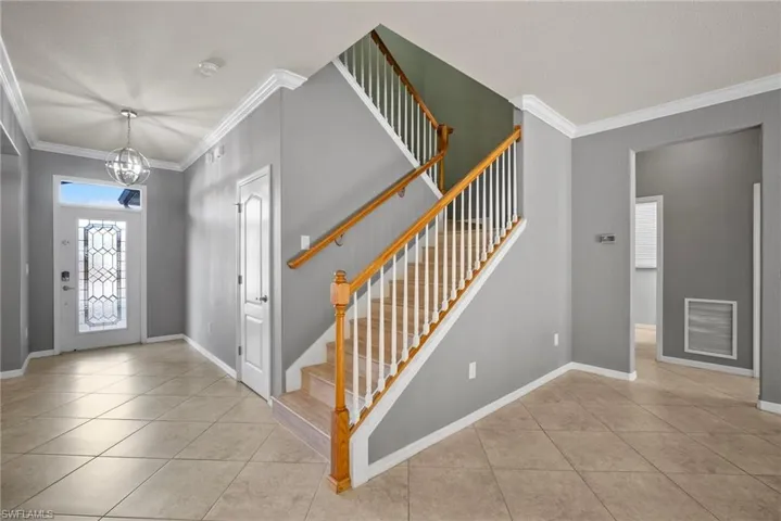 Tiled foyer entrance featuring crown molding and a chandelier