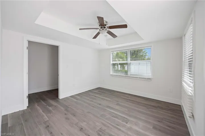 Unfurnished bedroom featuring a tray ceiling, baseboards, wood finished floors, and a ceiling fan