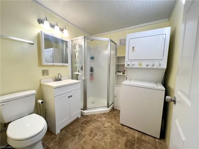 Full bath with a shower stall, toilet, vanity, and stacked washing maching and dryer