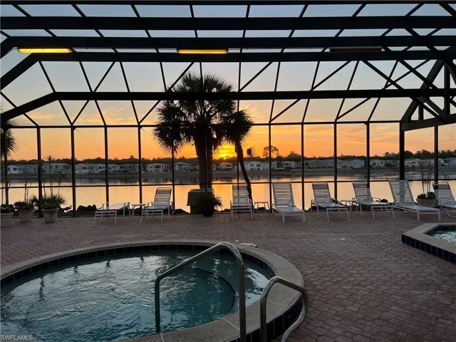 Pool at dusk featuring a lanai, a hot tub, and a water view