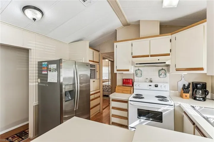 Kitchen featuring range hood, vaulted ceiling with beams, white range with electric cooktop, and stainless steel finish fridge/freezer