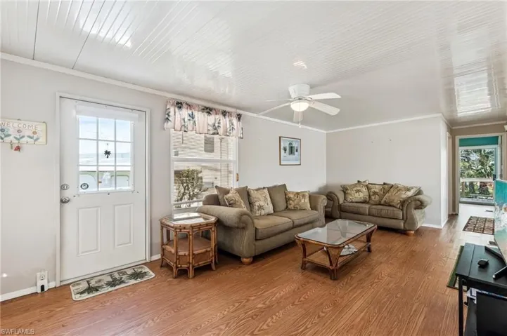 Living room featuring ceiling fan, baseboards, crown molding, and wood finish laminate floors