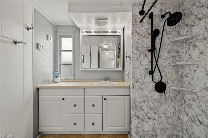 Bathroom featuring a textured ceiling, tiled shower, and vanity