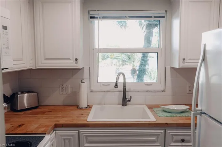 Kitchen with white cabinets, white appliances, and wood counters