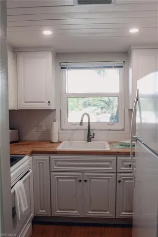 Kitchen featuring butcher block counters, freestanding refrigerator, white electric stove, white cabinetry, and backsplash