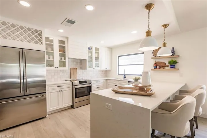 Kitchen with a kitchen breakfast bar, appliances with stainless steel finishes, pendant lighting, white cabinets, and recessed lighting