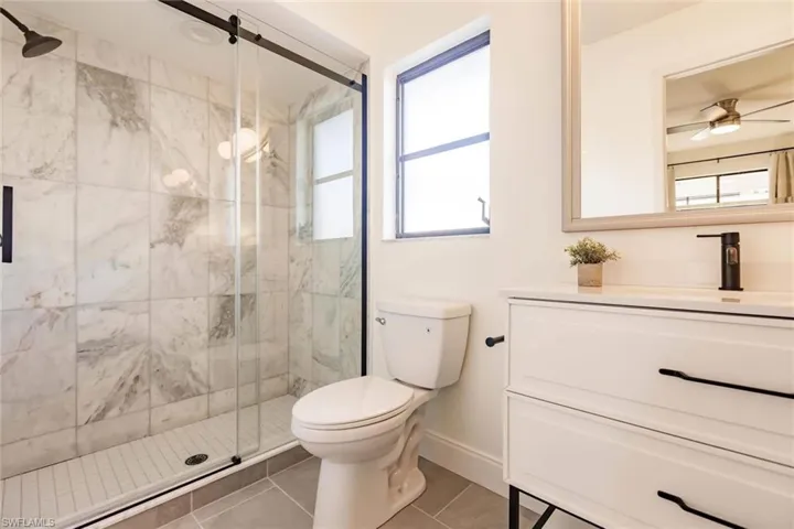 Bathroom with ceiling fan, vanity, light tile patterned floors, and a marble finish shower