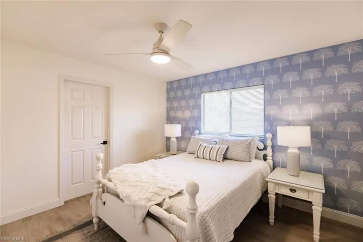 Bedroom featuring wood finished floors, wallpapered walls, a ceiling fan, and an accent wall