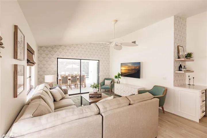 Living room with light wood-style flooring, vaulted ceiling, wallpapered walls, an accent wall, and ceiling fan