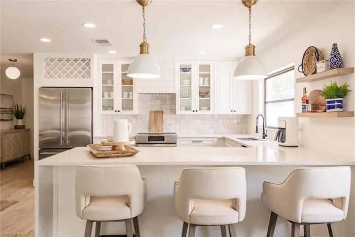 Kitchen with a kitchen bar, stainless steel appliances, decorative light fixtures, white cabinetry, and light stone countertops