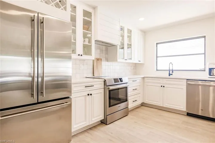Kitchen with stainless steel appliances, white cabinets, glass insert cabinets, and recessed lighting