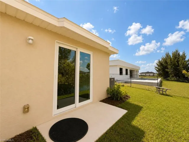 Exterior patio with sliding glass doors, stucco finish, and an expansive lawn