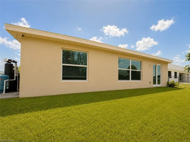 Expansive green lawn with a stucco exterior, multiple windows, and a glass sliding door