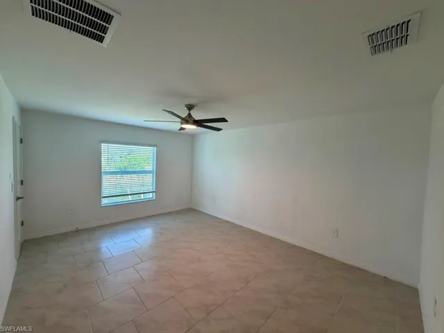 Spacious room featuring neutral-toned tile flooring, a window with blinds, a ceiling fan with integrated lighting, and white walls