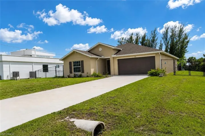 Contemporary stucco exterior with a brown garage door, featuring a concrete driveway, established lawn, and a partial black chain-link fence