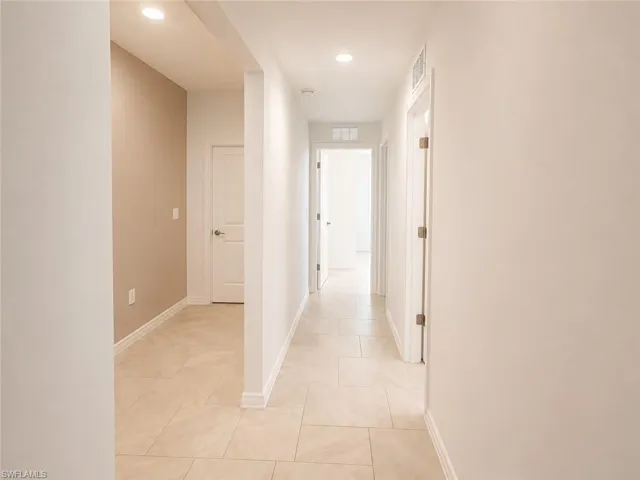 Hallway featuring neutral-toned tile flooring, recessed lighting, and crisp white trim