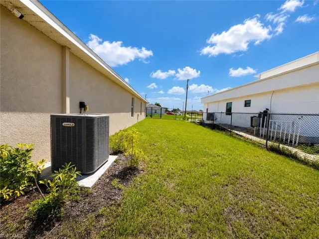 Expansive grassy side yard featuring a Lennox HVAC unit, stucco exterior, and a chain-link fence
