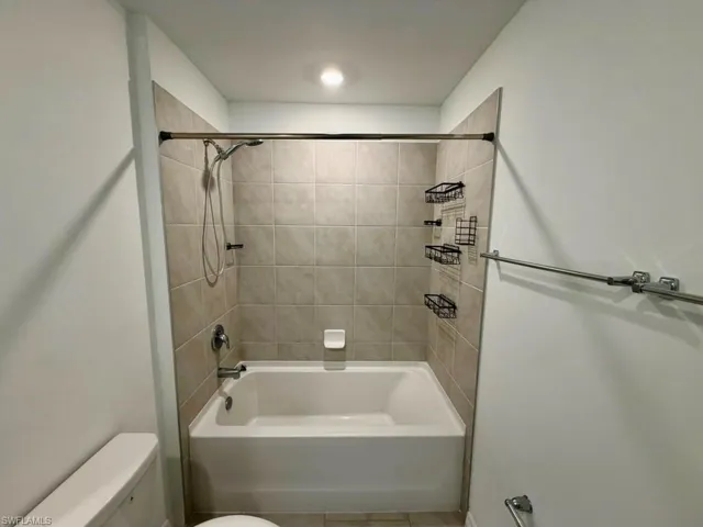 Bathtub and shower combination featuring neutral-toned tile surround, chrome fixtures, and recessed ceiling lighting