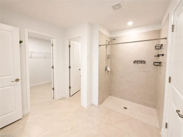 Spacious bathroom featuring a walk-in shower with light-toned wall tiling, a handheld showerhead, and recessed lighting