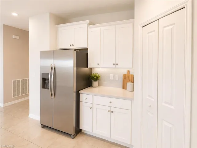 Kitchen area featuring white shaker-style cabinetry, a built-in stainless steel side-by-side refrigerator, light-toned countertops, and a white subway tile backsplash