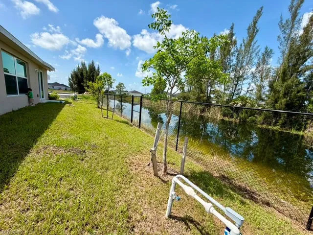 Expansive grassy yard with a black chain-link fence bordering a natural water feature