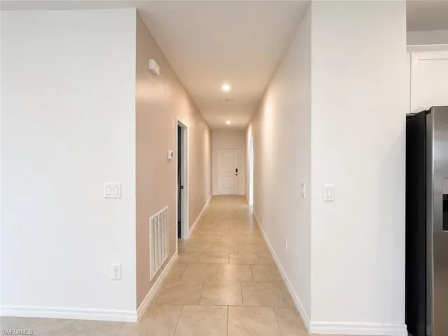 Long hallway featuring neutral-toned tile flooring, recessed lighting, and white baseboards
