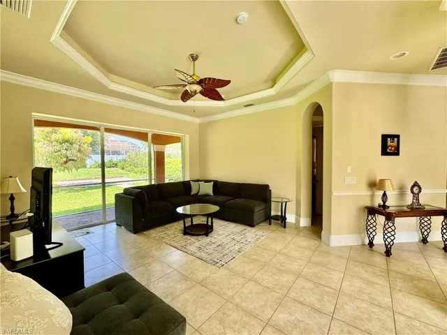 Living area featuring arched walkways, ceiling fan, a tray ceiling, ornamental molding, and light tile patterned flooring