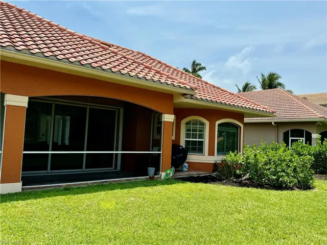 Rear view of property featuring a yard, stucco siding, a tiled roof, and a sunroom
