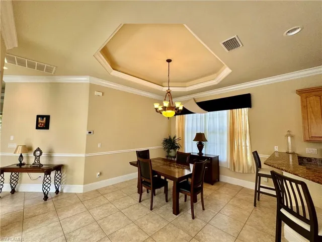 Dining area featuring hanging lights, crown molding, a tray ceiling, and light tile patterned flooring