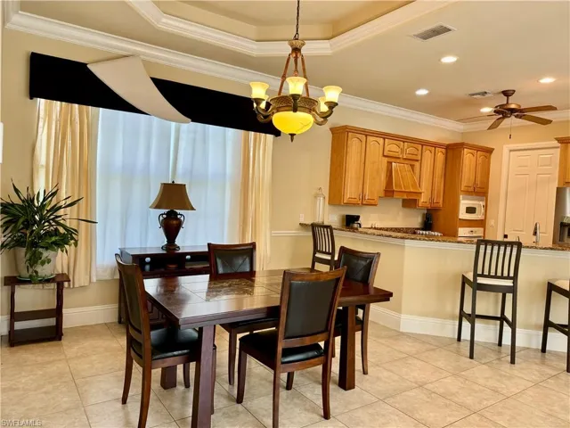 Dining space with crown molding, hanging lights, a ceiling fan, light tile patterned floors, and a tray ceiling