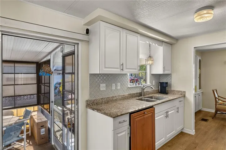 Kitchen with stone counters, a sink, white cabinets, hanging light fixtures, and tasteful backsplash