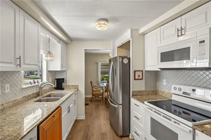 Kitchen featuring pendant lighting, white cabinetry, a sink, light stone countertops, and white appliances