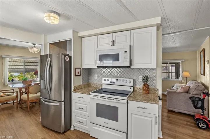 Kitchen with open floor plan, white appliances, light wood-type flooring, and white cabinetry