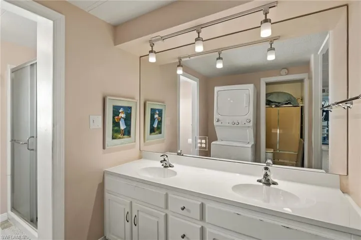 Full bath with double vanity, stacked washer / dryer, a sink, and a shower stall