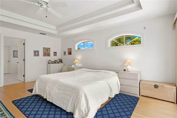 Bedroom with light hardwood / wood-style floors, ceiling fan, crown molding, and a tray ceiling