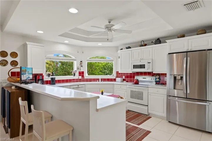 Kitchen featuring a tray ceiling, tasteful backsplash, white cabinets, white appliances, and ceiling fan