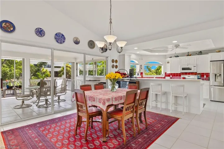Tiled dining area featuring ceiling fan with notable chandelier, a raised ceiling, and high vaulted ceiling