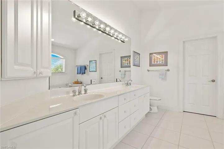 Bathroom featuring toilet, lofted ceiling, double sink vanity, and tile patterned flooring