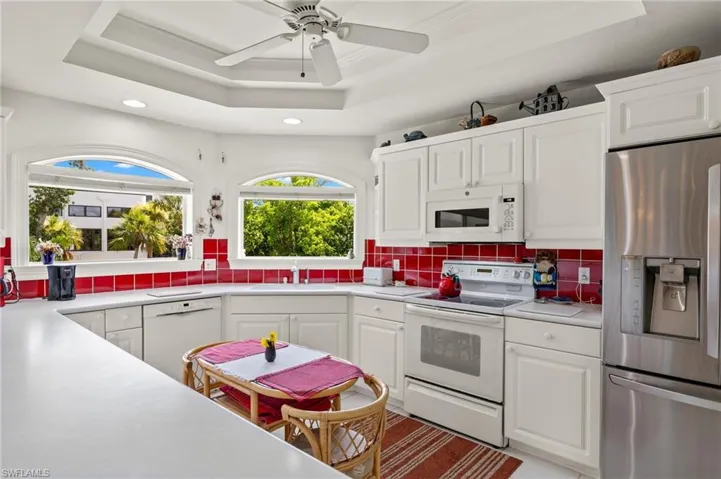 Kitchen with a raised ceiling, white cabinetry, backsplash, and white appliances