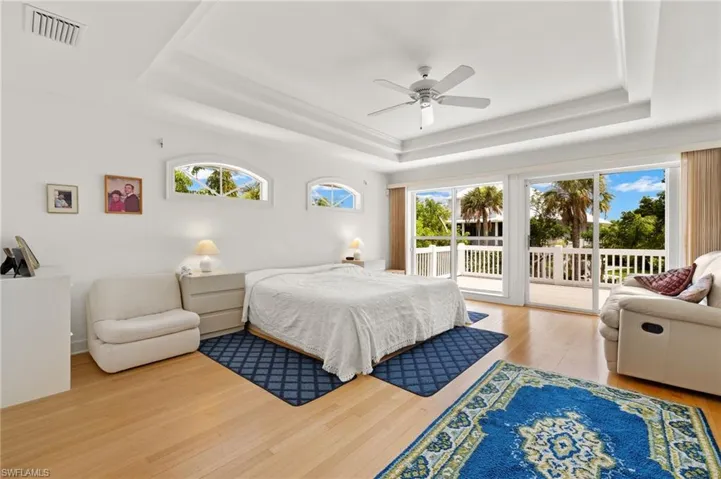 Bedroom featuring a raised ceiling, light hardwood / wood-style flooring, ceiling fan, and access to exterior