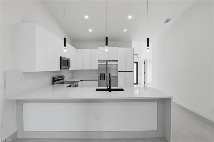 Kitchen featuring modern cabinets, hanging light fixtures, a peninsula, white cabinets, and stainless steel appliances