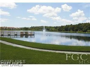 Serene lake with a central fountain, bordered by a wooden dock structure and a paved pathway