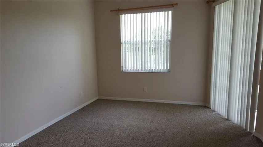 Carpeted room featuring a window with vertical blinds and a sliding glass door with vertical blinds