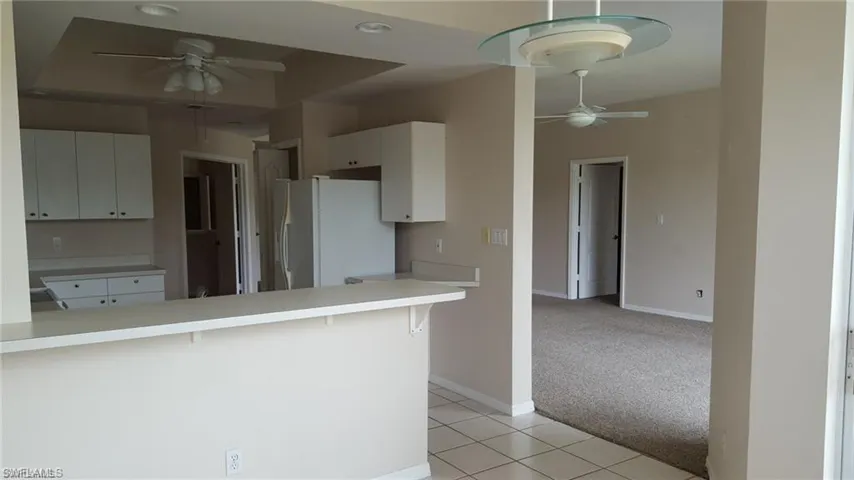 Kitchen featuring white cabinetry and countertops, a peninsula with breakfast bar seating, tile flooring, and a ceiling fan with light fixture