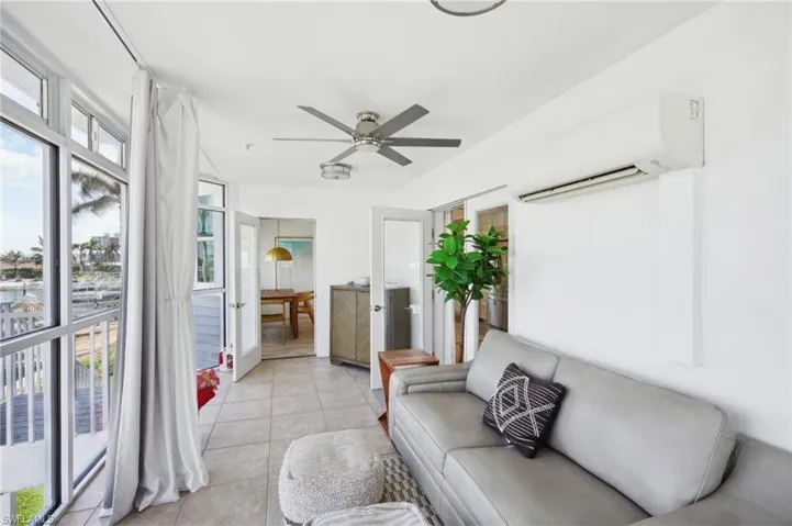 Living room with ceiling fan, light tile patterned flooring, and a wall mounted air conditioner