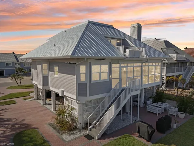 Back house at dusk featuring a sunroom, a balcony, a patio, and a carport