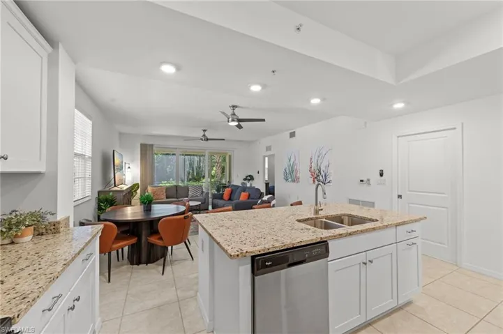 The property features a kitchen with granite countertops, white cabinetry, and a stainless steel dishwasher, opening to a living area with tile flooring and a view of exterior landscaping