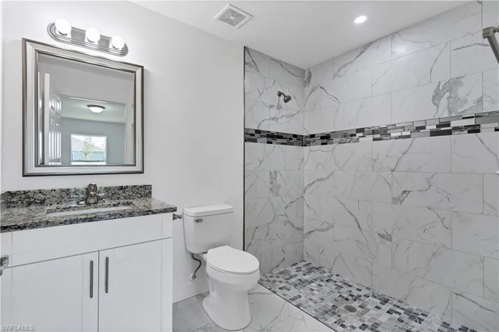 Bathroom featuring tiled shower, vanity, and toilet