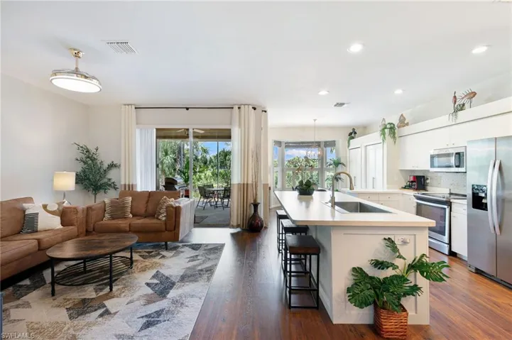 Kitchen featuring dark wood finished floors, a kitchen bar, appliances with stainless steel finishes, a sink, and hanging light fixtures