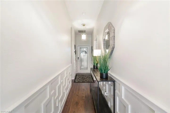 Doorway to outside with a decorative wall, dark wood-style flooring, wainscoting, and visible vents